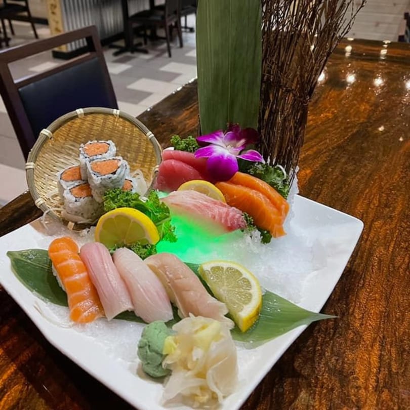 A sushi and sashimi platter with rolls, nigiri, and raw fish, garnished with lemon and a purple orchid.