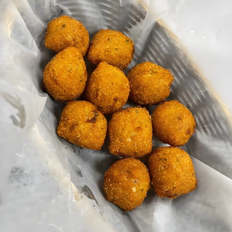 Golden-brown hush puppies, a classic seafood side, served in a paper-lined basket.