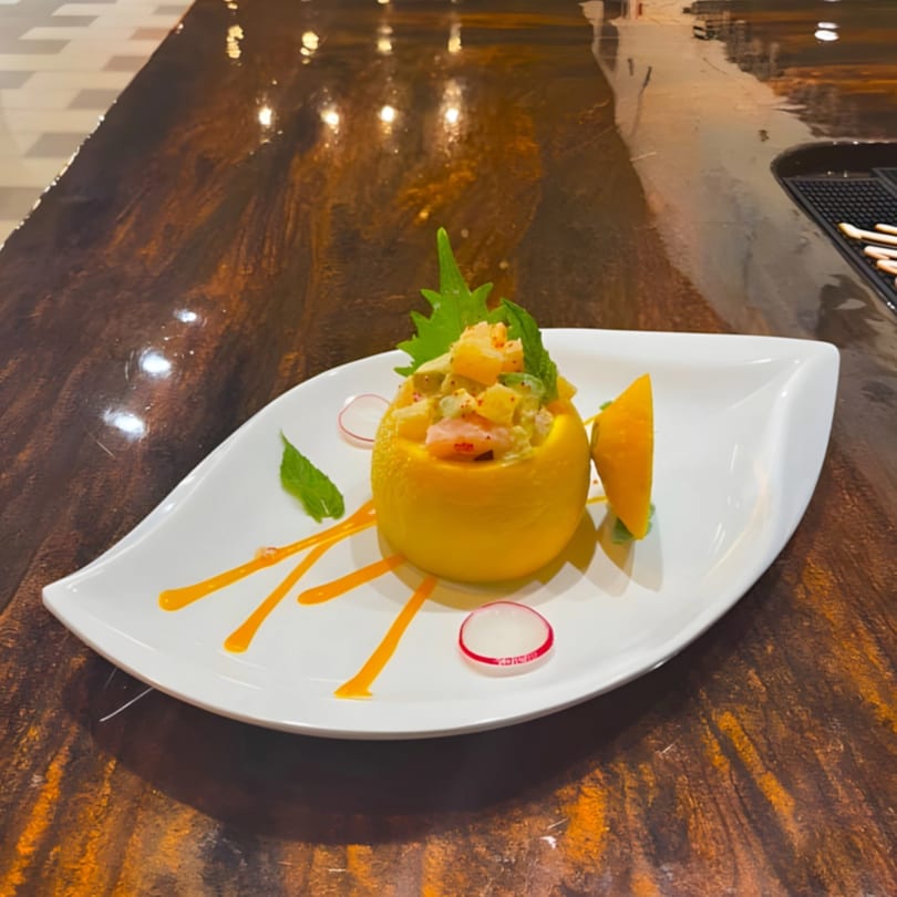 Seafood salad in a hollowed-out lemon, garnished with mint, radish, and mango on a white plate.