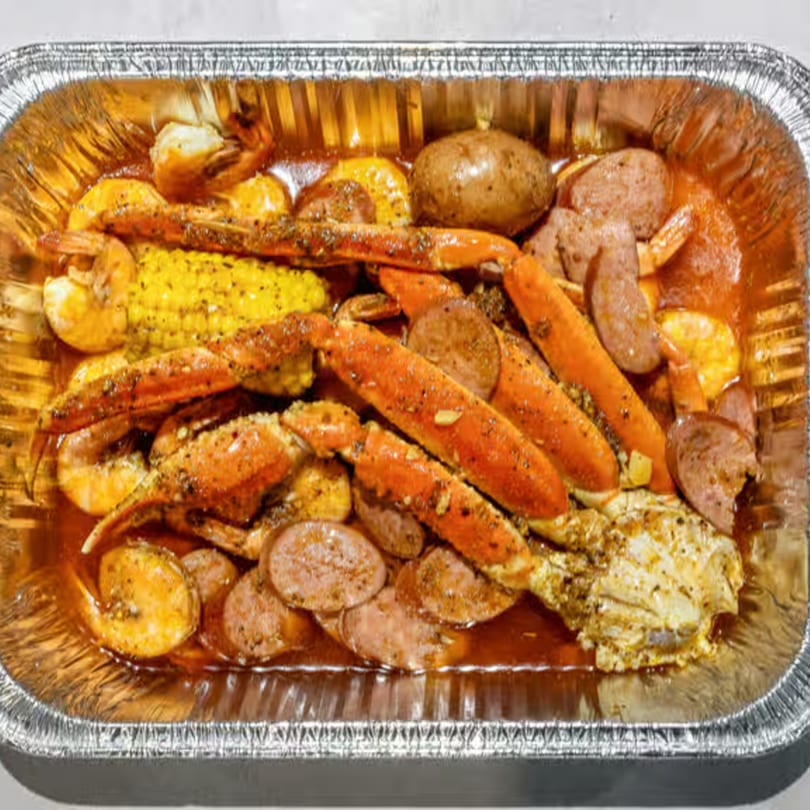 King Ocean Crab's seafood boil with crab legs, shrimp, sausage, corn, and potatoes in a foil pan.